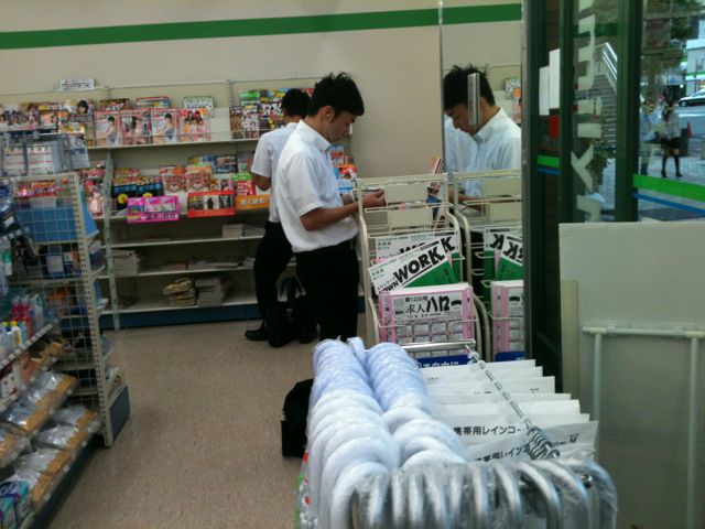 Convenience stores and grocery store sell magazines. Men sometimes stop by to read magazines on their way to work or when going home. In this photo, both men are reading magazines on their way home from work. The time is 18:00 Japan Standard Time. Intelligent as always, Japan has forsaken day light saving time.