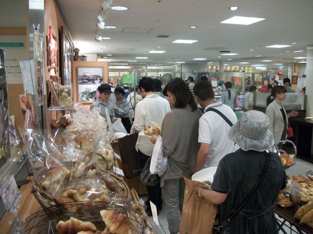 Customers quietly wait in line to purchase a very popular red bean pastry at a food specialty shop located in a Japanese department store. The queue emits quiet conversations and muted laughter. Many department stores offer complete grocery stores plus independent vendors with specialty products.