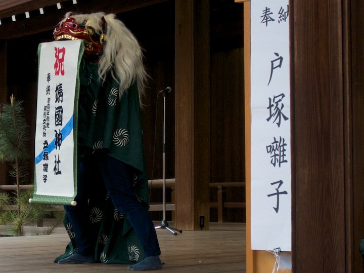 Toward the end of a lion dance, the lion picks up a scroll with its mouth--a pretty difficult task--and unrolls a message of good luck. This lion dances at Yasukuni Shrine, Tokyo, Japan.